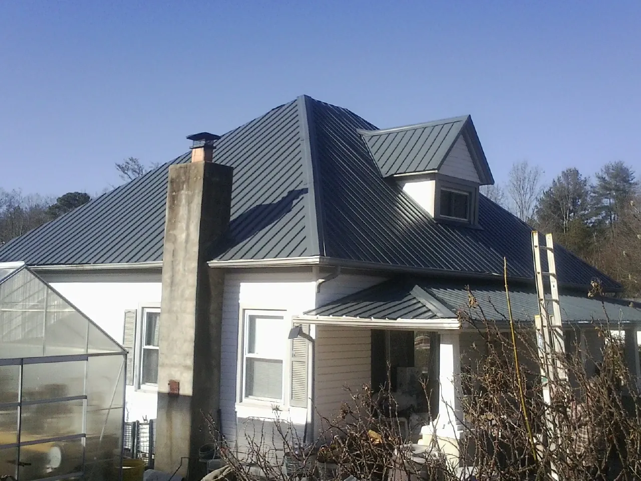 Dark blue standing seam metal roof on a white farmhouse with dormer — Slate & Tile Roof Repair by Roofing Brothers in Plattsburgh