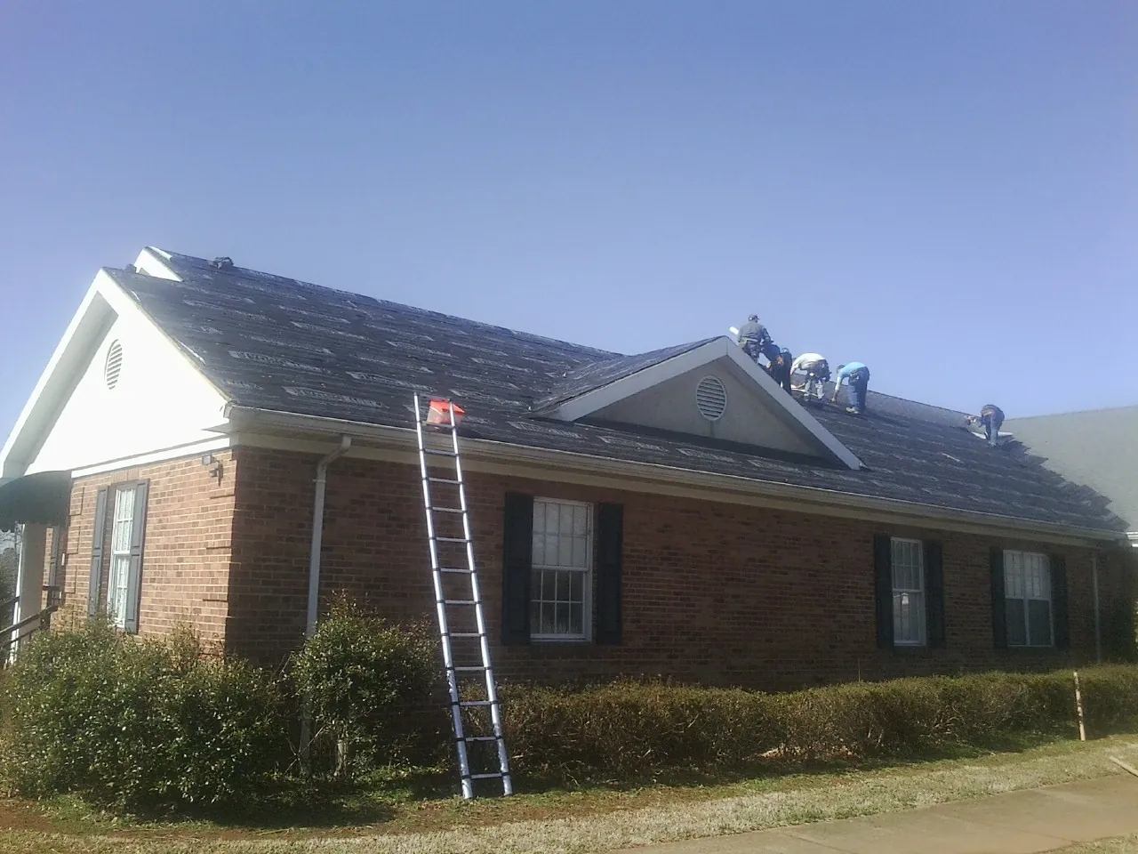 Crew tearing shingles off a brick ranch roof with a ladder set — Emergency Roof Repair work by our crew in Plattsburgh