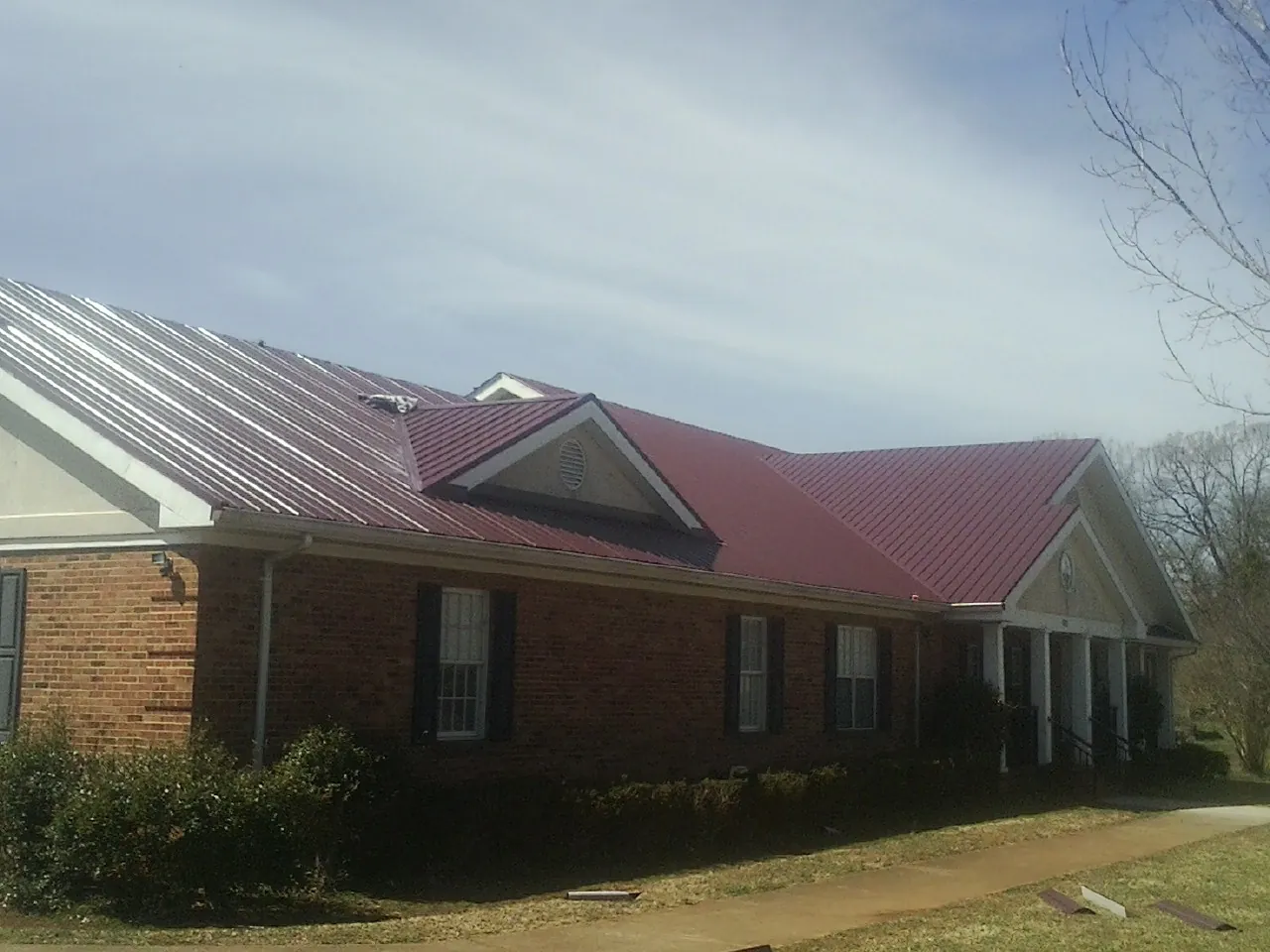 Red metal roof with gabled entries on a long brick building, from a Hail Damage Roof Repair job in Plattsburgh