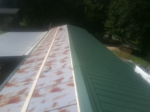 Old rusted panels beside newly installed green metal roofing — Wind Damage Roof Repair by Roofing Brothers in Plattsburgh