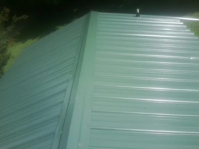 New green metal panels meeting at the ridge of a roof — Flat Roof Repair work by our crew in Plattsburgh