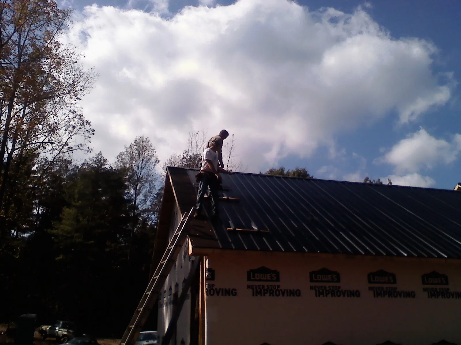 Roofer fastening dark metal panels high against a cloudy sky, from a Roof Inspection job in Plattsburgh