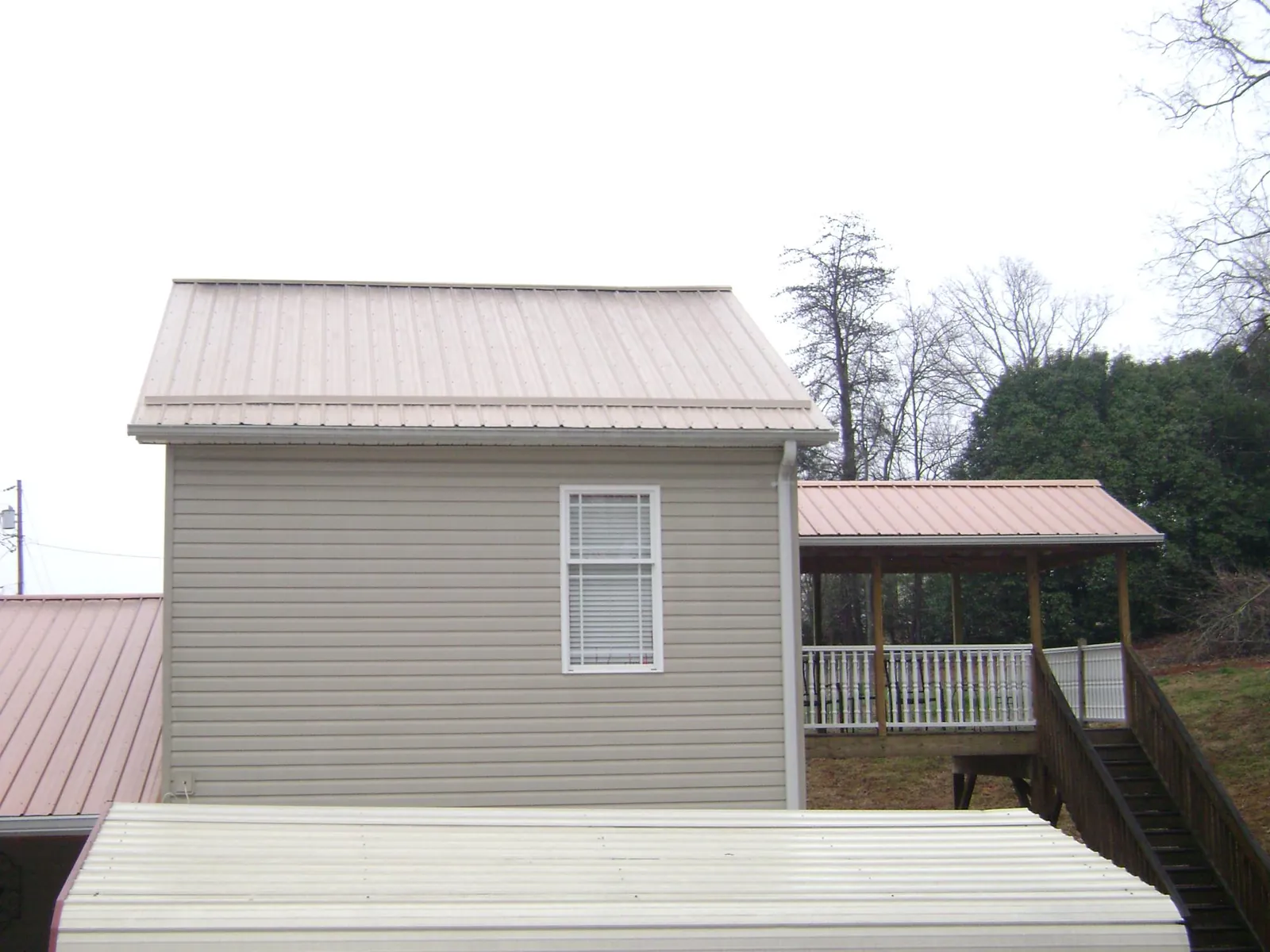 Tan metal roofs on a two story addition and attached porch, from a Roof Replacement job in Plattsburgh